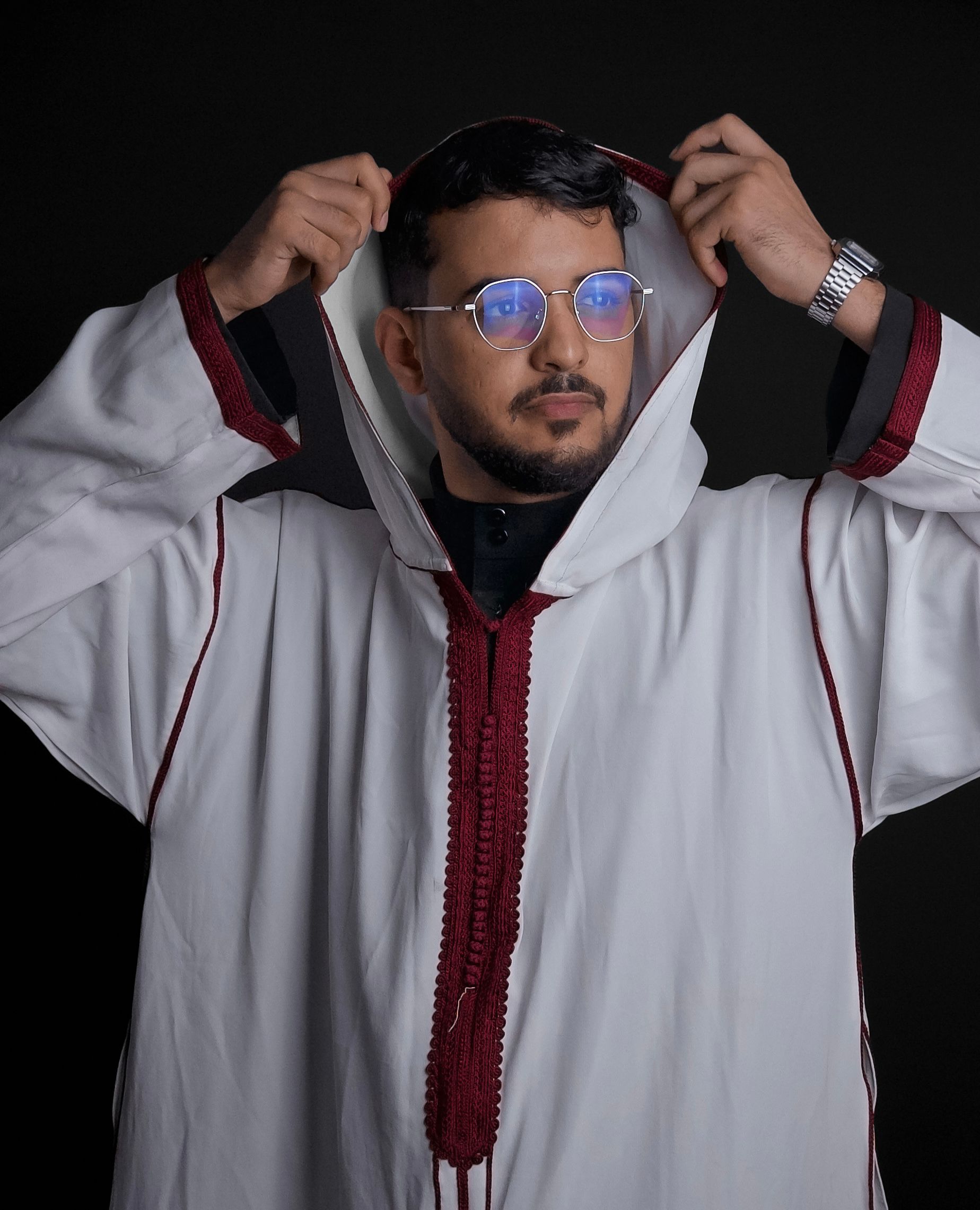 Stylish man wearing traditional djellaba with glasses in a studio setting.